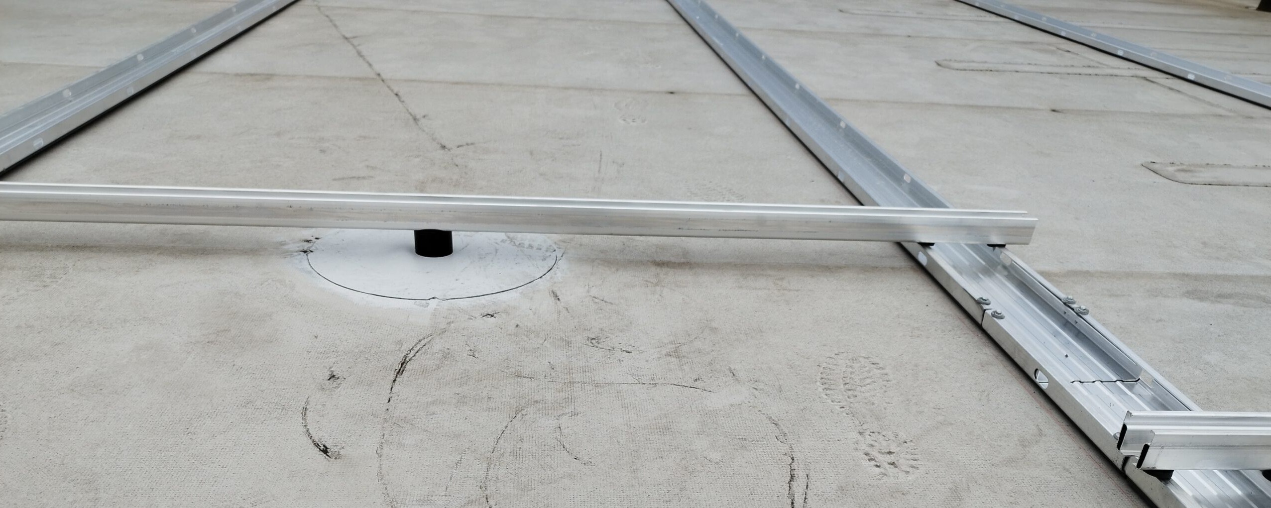Parallel ausgelegte Aluminiumprofile zur Vorbereitung eines Montagerasters auf heller Dachabdichtung