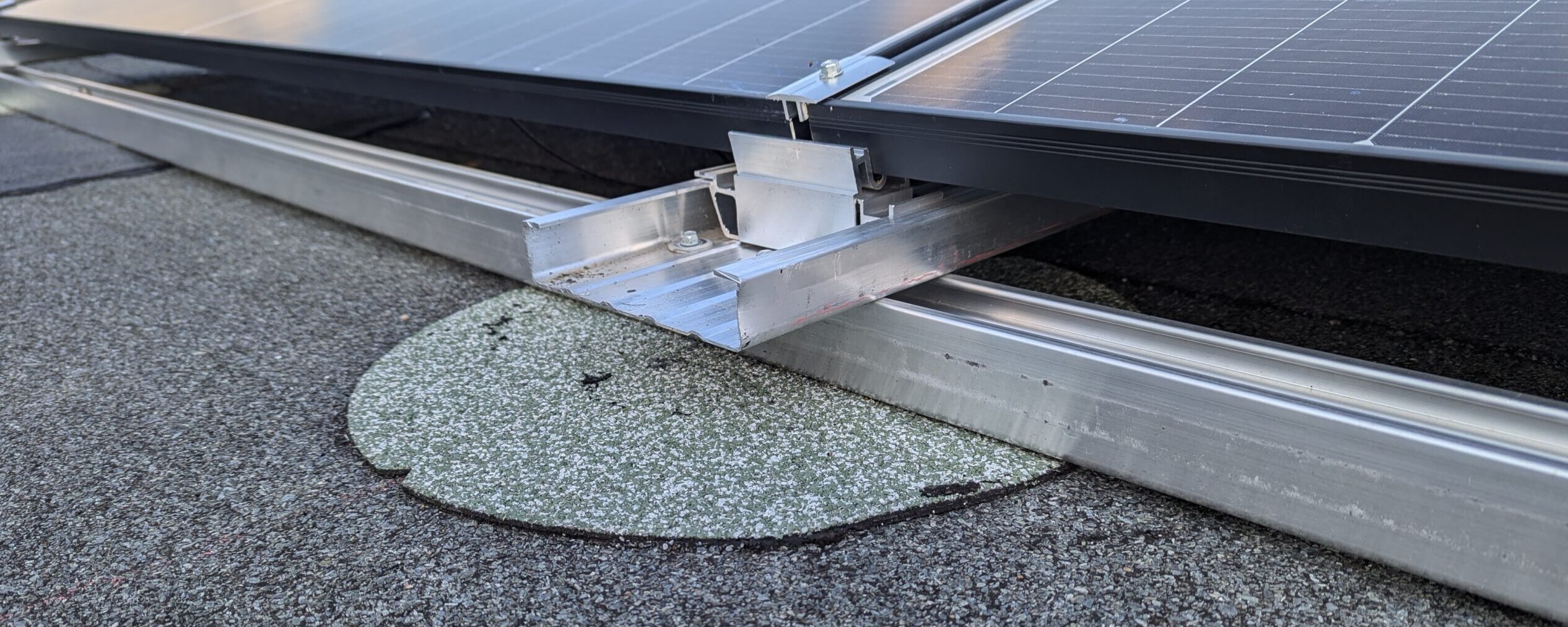 Seitlicher Blick auf das Tragprofil eines Solarmoduls über einer runden Schutzauflage auf dem Flachdach